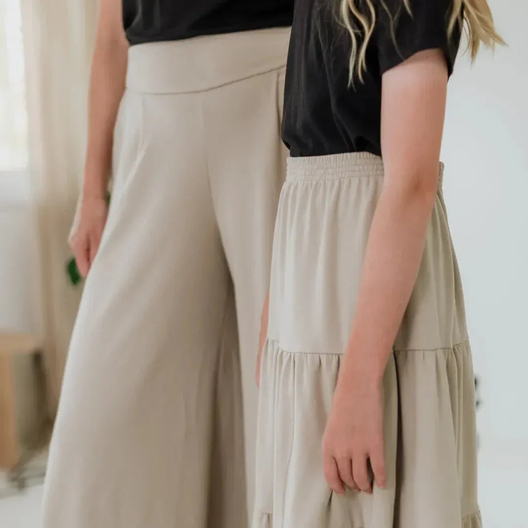 Girl in beige bamboo skirt and woman in beige pants, both in black tops indoors