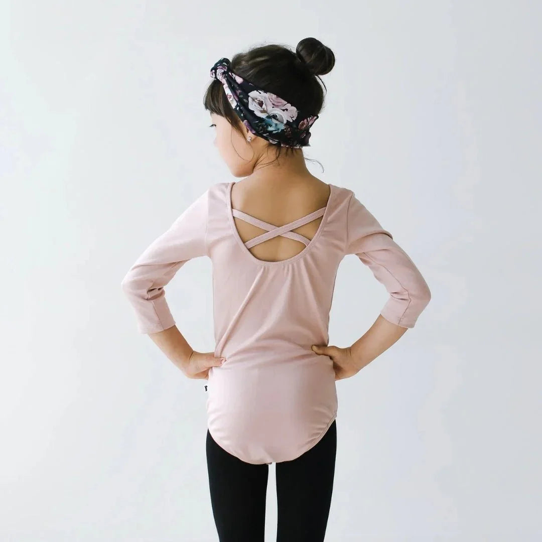 Girl in pink bamboo Audrey bodysuit with floral headband, hands on hips, facing back