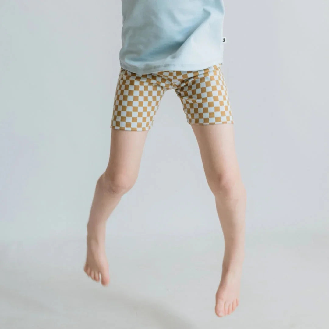 Child wearing brown and white checkerboard shorts jumping in a minimalist studio