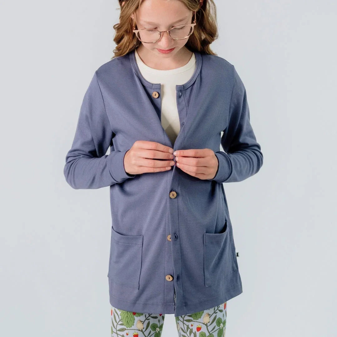 Girl in glasses wearing blue cardigan and floral leggings buttoning sweater