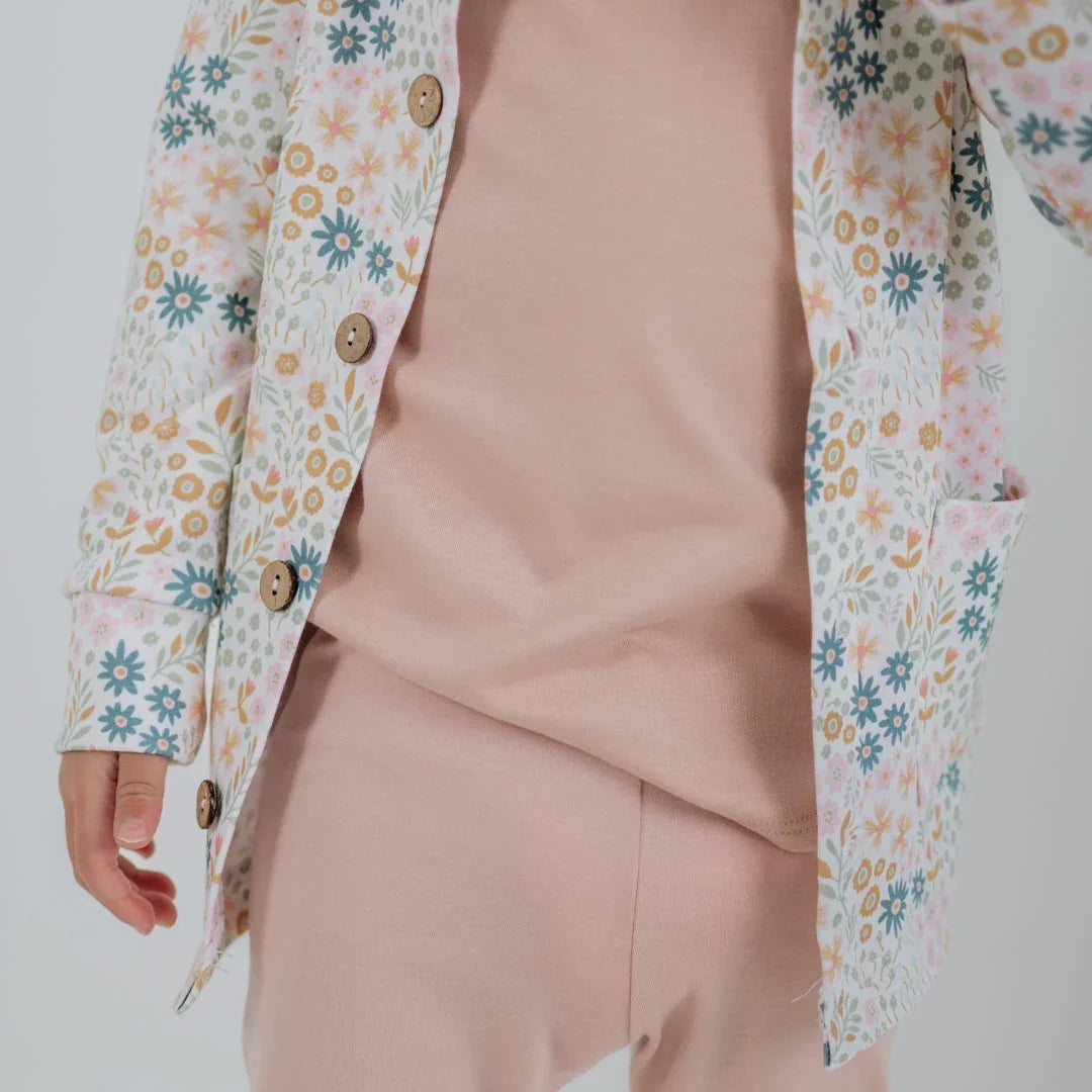 Child in pastel pink outfit with floral print jacket featuring wooden buttons