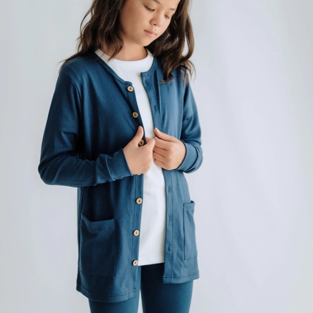 Girl wearing blue cardigan with buttons and pockets over white shirt, plain background