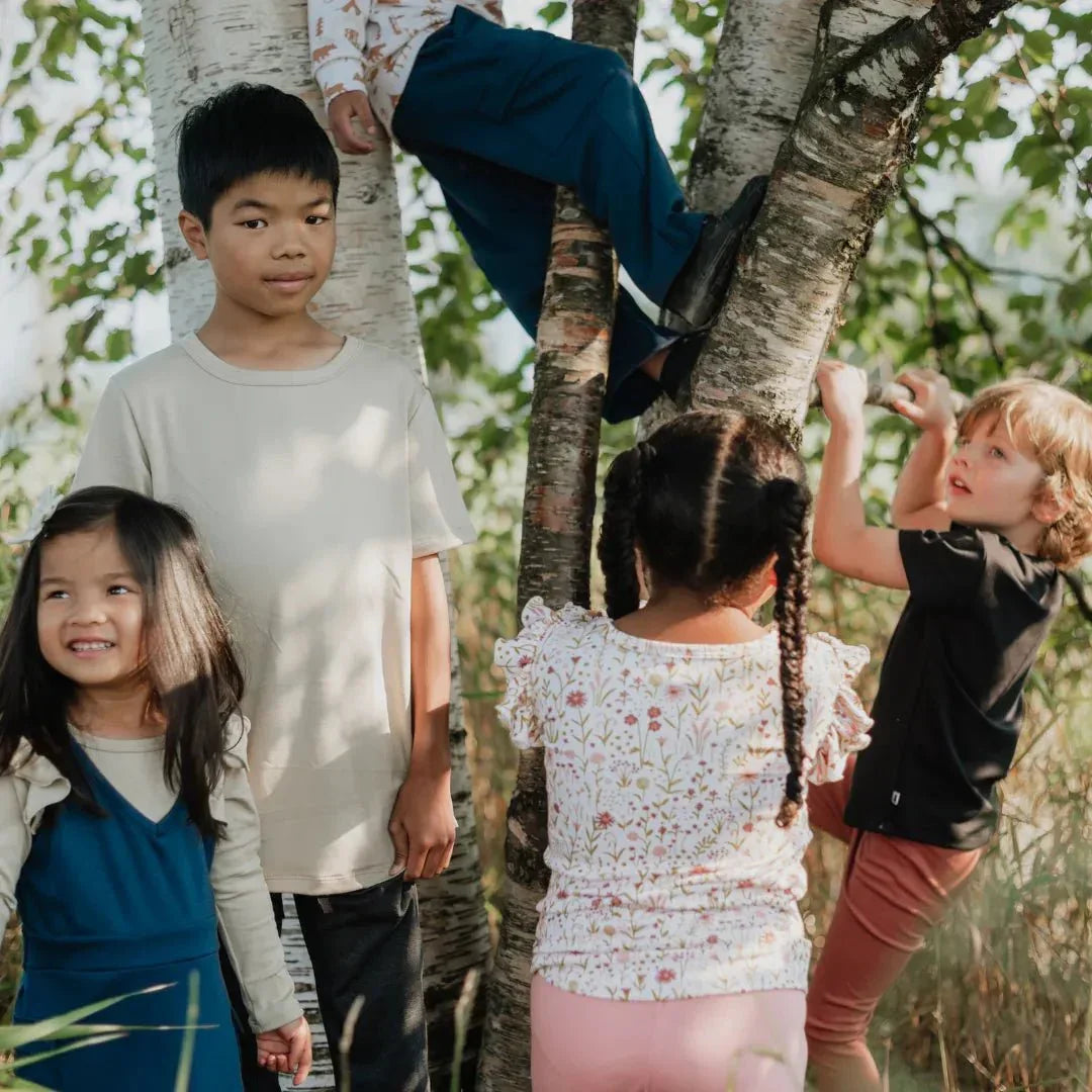 Group of children in colorful outfits playing and climbing birch trees outdoors