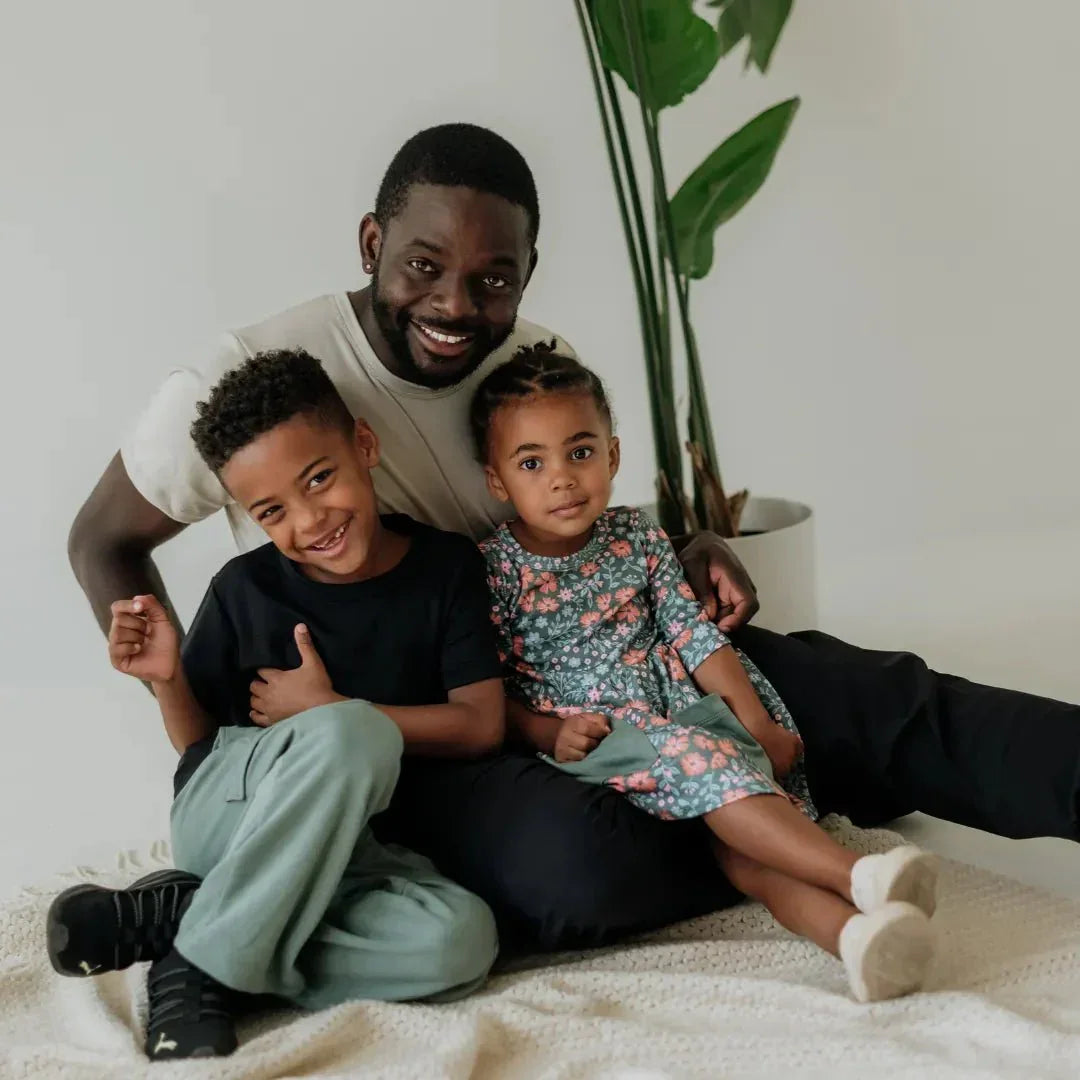 Smiling family with man, boy in green bamboo cargo pants, and girl in floral dress indoors