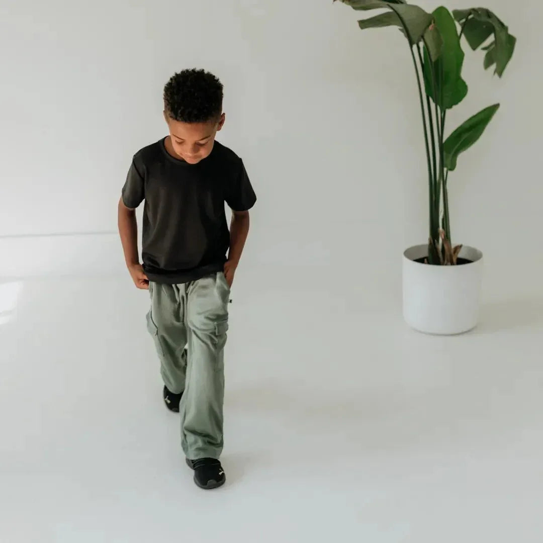Boy in bamboo cargo pants and black t-shirt walking in minimalist room with potted plant