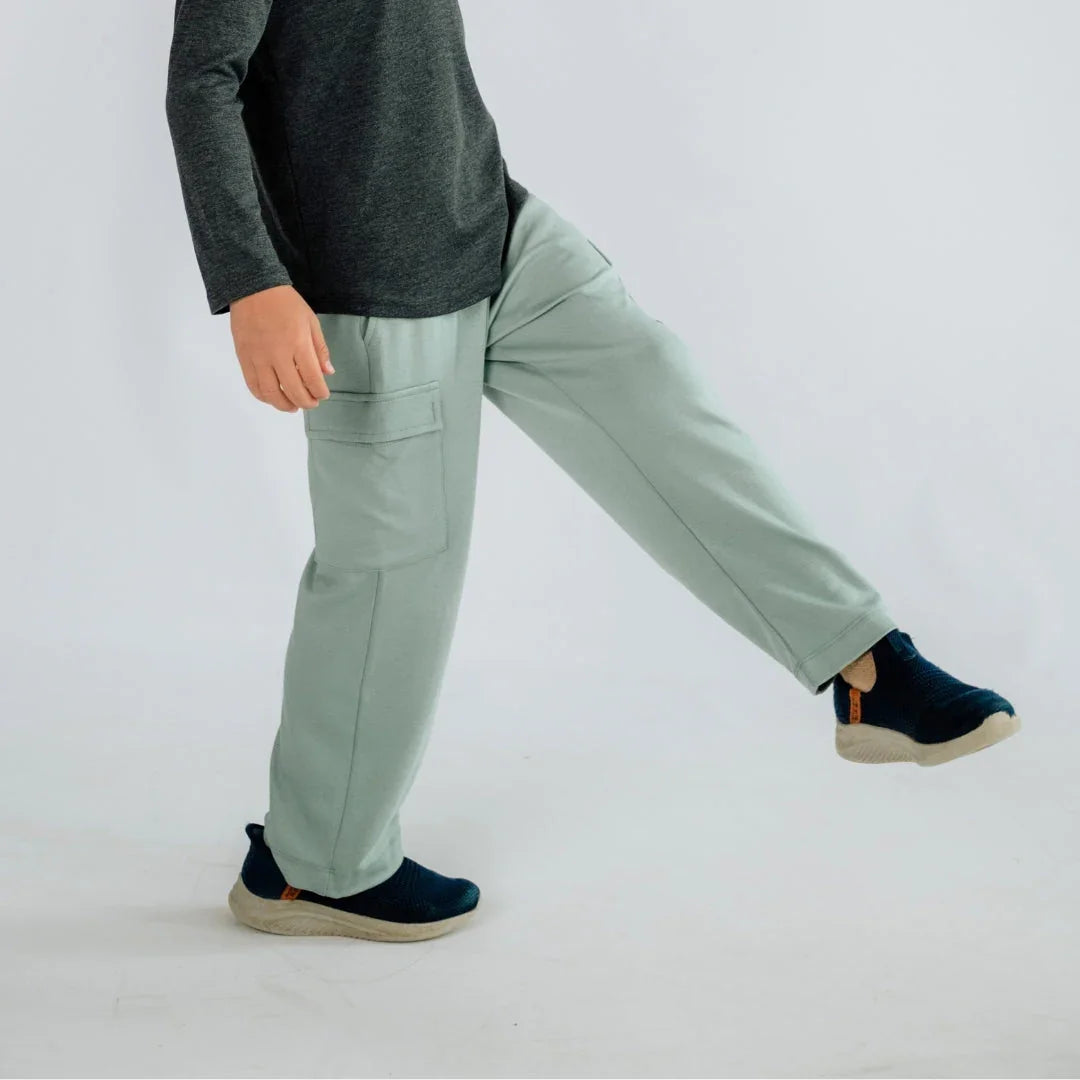 Kid wearing light green cargo pants and dark sneakers on a white background