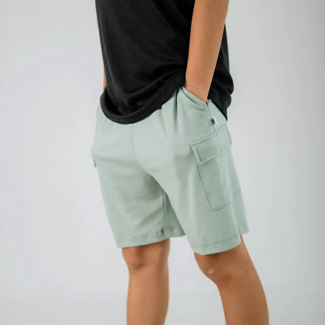 Youth light green cargo shorts with side pockets, worn with black t-shirt, studio background