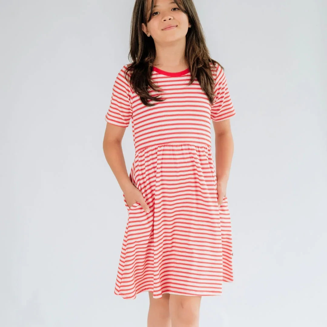 Girl wearing red and white striped short sleeve youth dress with pockets against plain background.