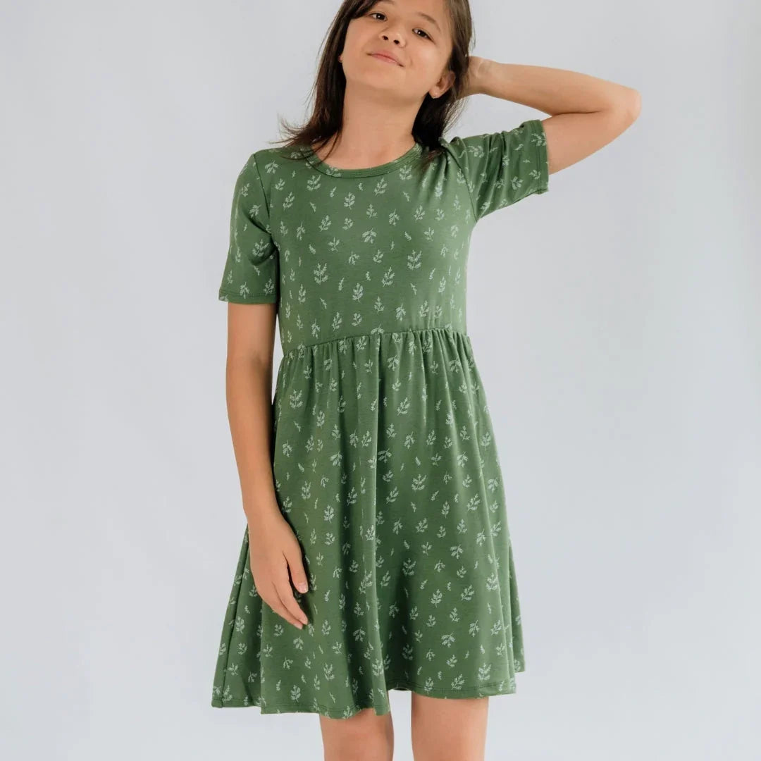 Girl wearing a green short sleeve dress with white leaf print, standing against plain background