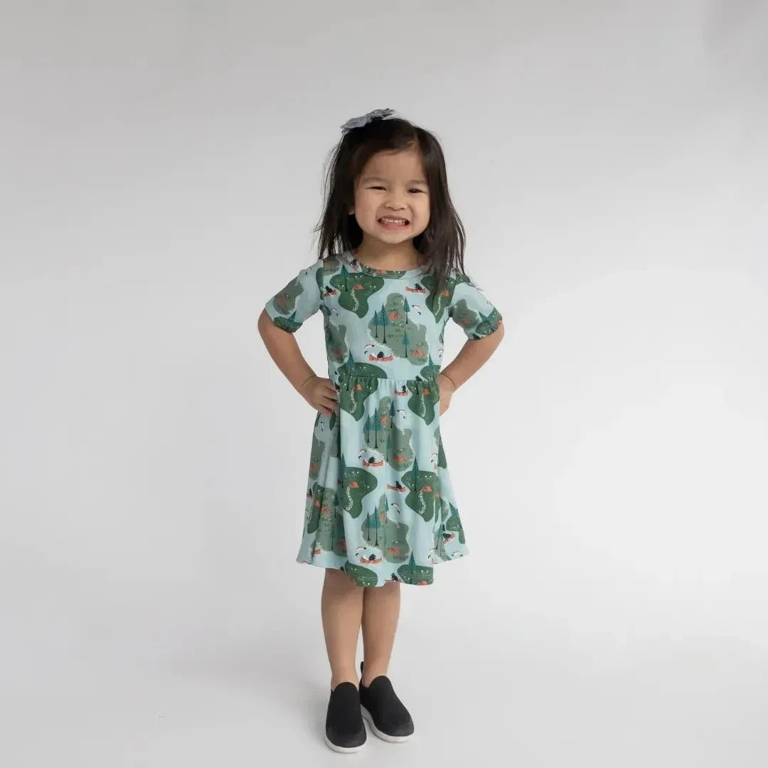 Smiling girl in a green patterned bamboo Daphne dress, standing in a studio.