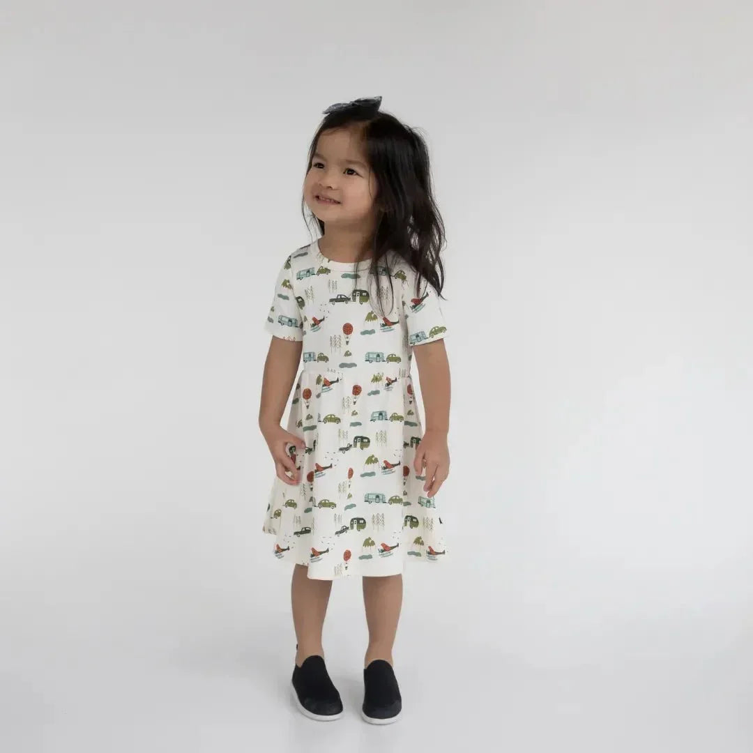 Young girl wearing a white bamboo Daphne dress with colorful car and airplane prints