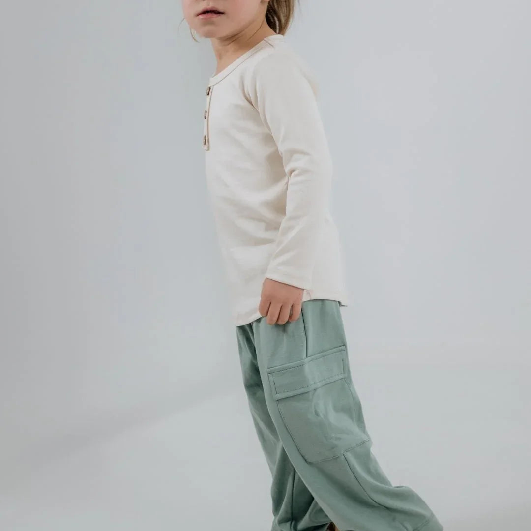 Child wearing a cream bamboo henley long sleeve shirt and sage cargo pants, standing indoors