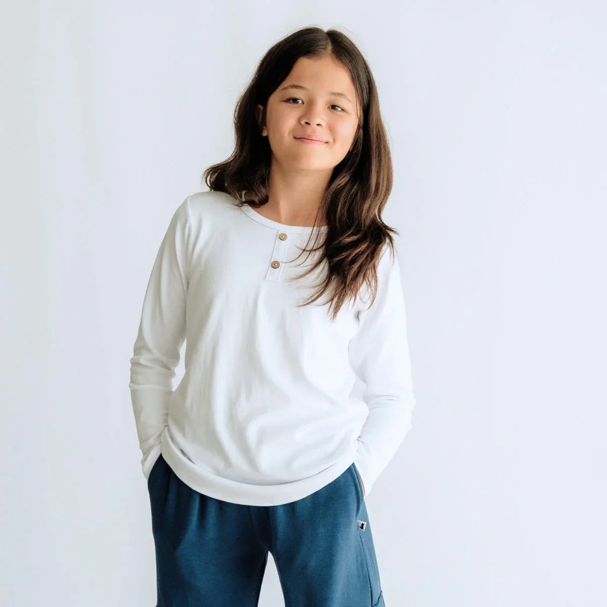Smiling child in white long sleeve henley shirt and blue pants on plain background