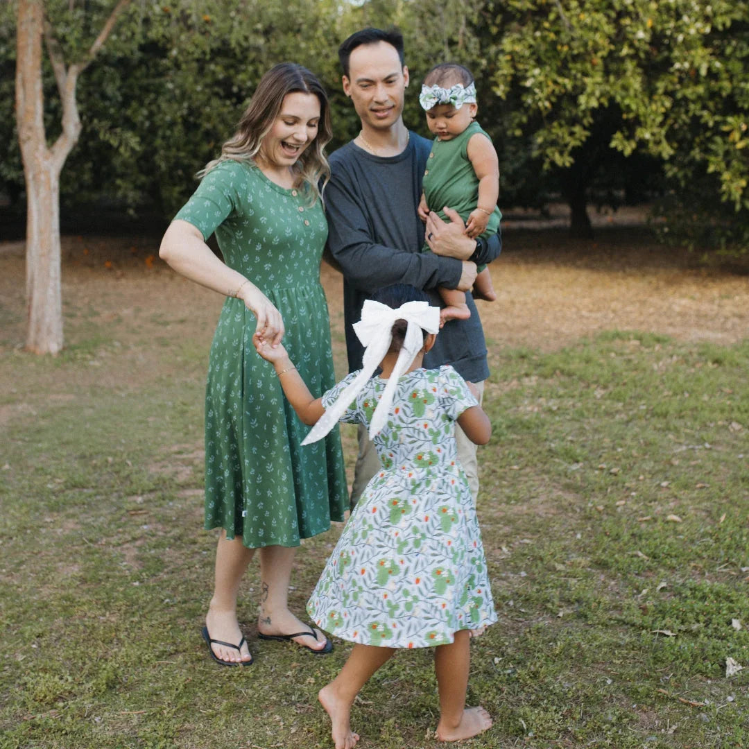 Family playing outdoors, woman in green dress, man holding baby, girl with white bow in hair