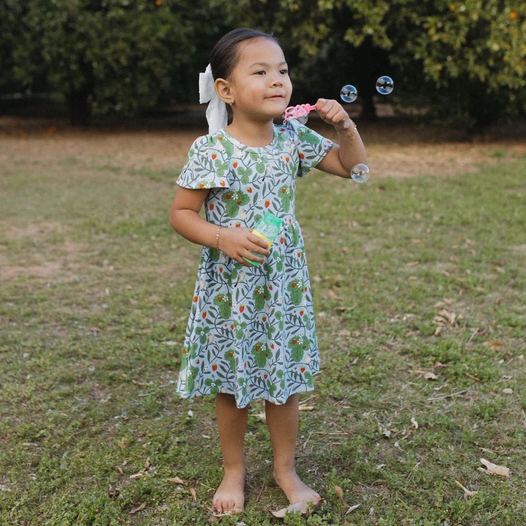 Young girl in a floral dress blowing bubbles outdoors on green grass