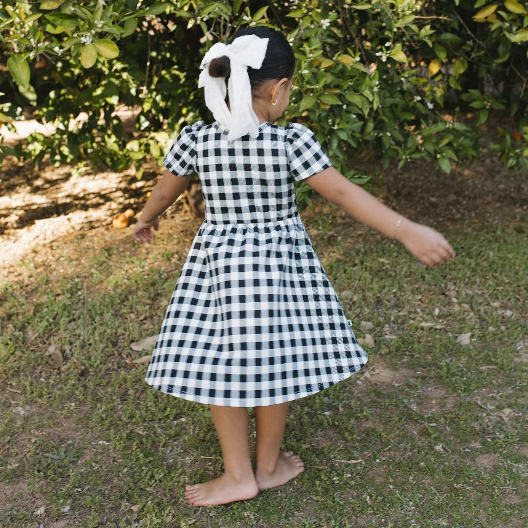 Girl in gingham dress with white bow in hair twirling barefoot outdoors