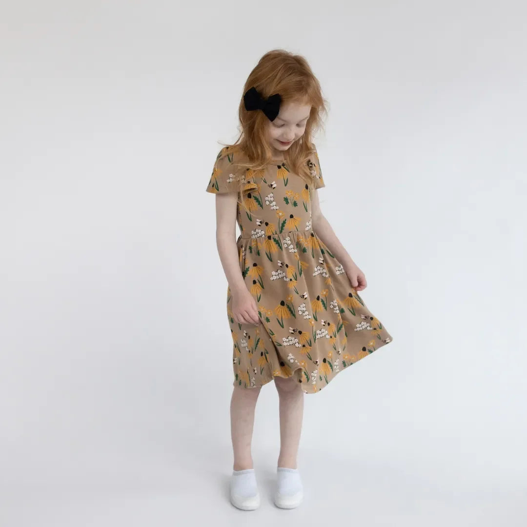 Girl in mustard yellow floral dress with black hair bow on plain white background