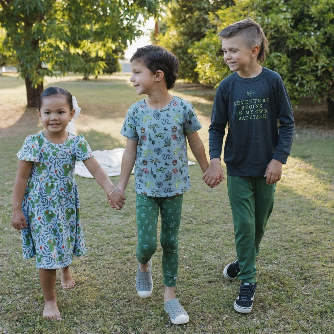 Three kids in whimsical nature-inspired outfits holding hands outdoors on green grass