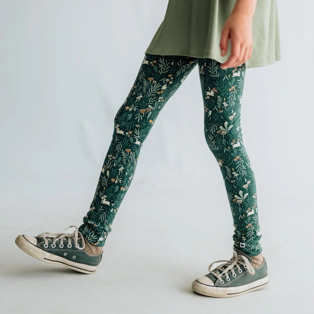 Child wearing green botanical print leggings and sneakers against a plain background