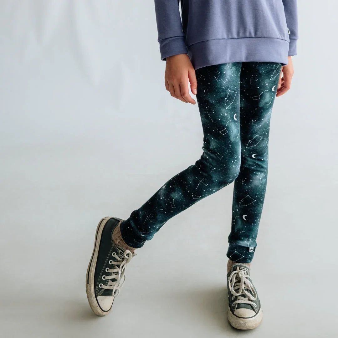 Child wearing star constellation print leggings, blue sweater, and sneakers on white background