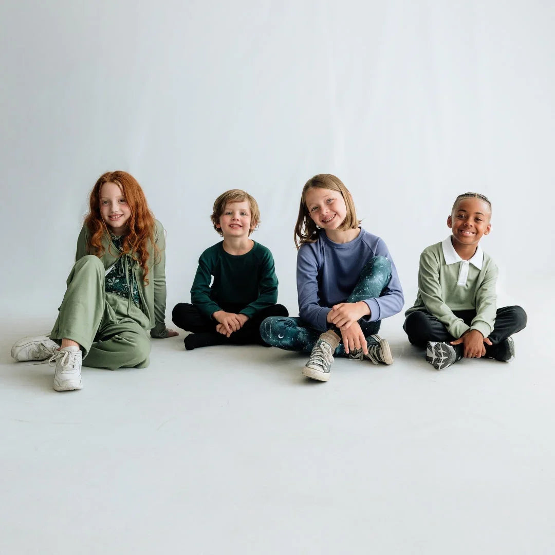 Four happy kids in colorful casual outfits sitting on a white studio floor