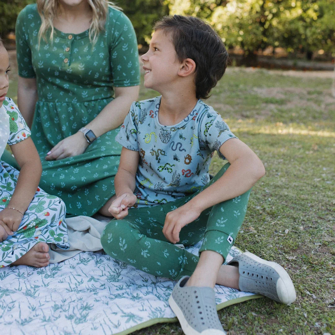 Children and woman in patterned green outfits sitting on a picnic blanket outdoors