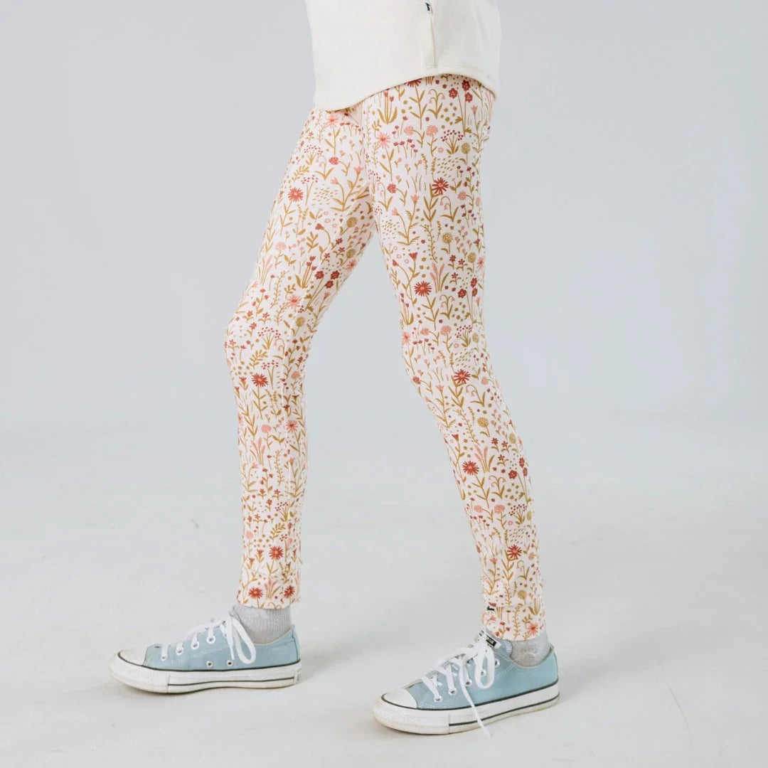 Child wearing cream floral leggings and blue sneakers on a plain background