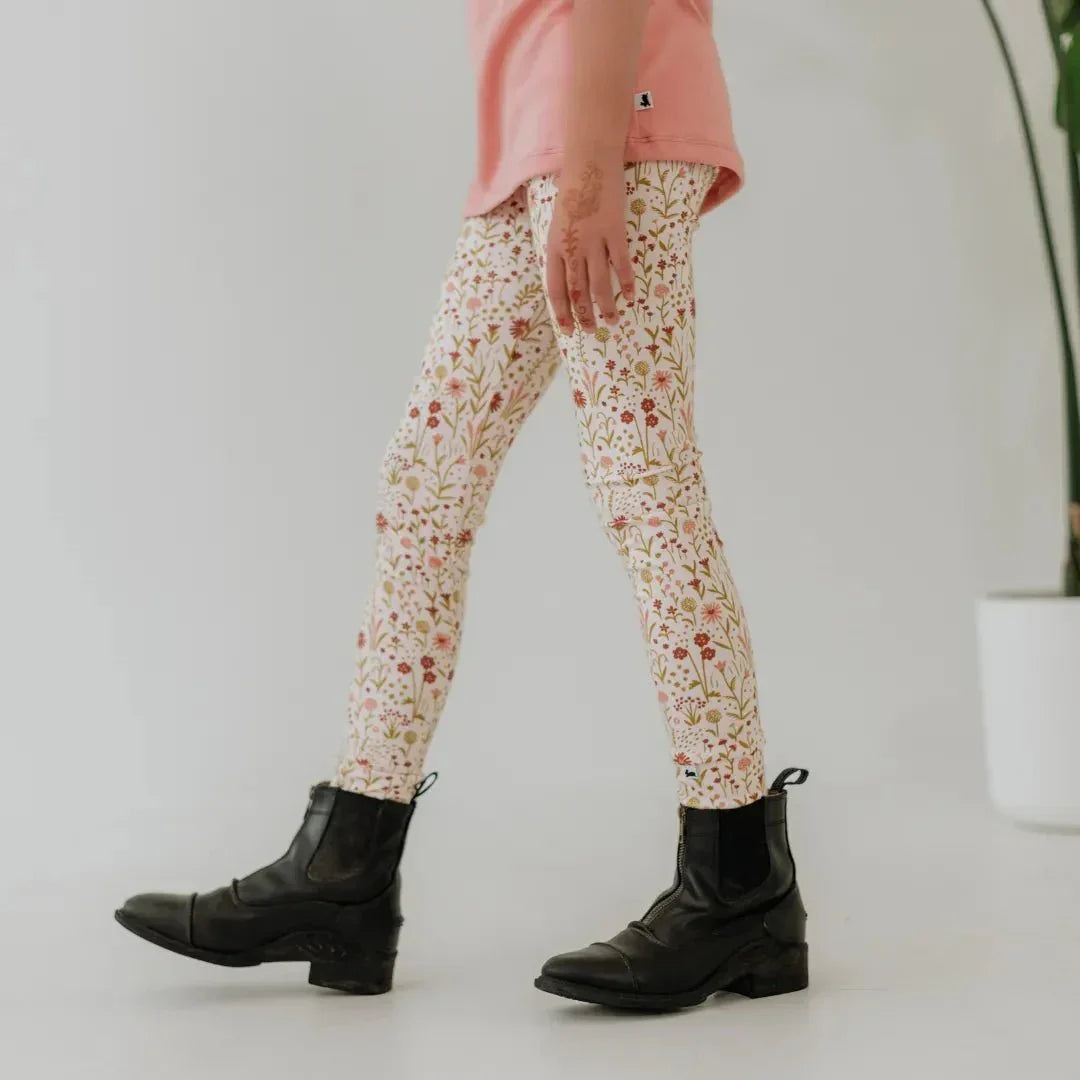 Child wearing floral bamboo leggings and black boots, pink top, indoor minimal setting