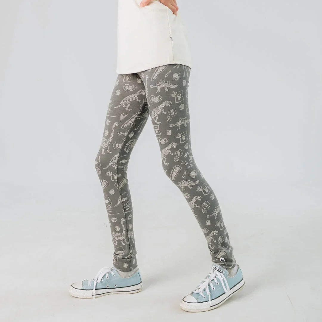 Child wearing gray bamboo leggings with dinosaur print and blue sneakers on white background