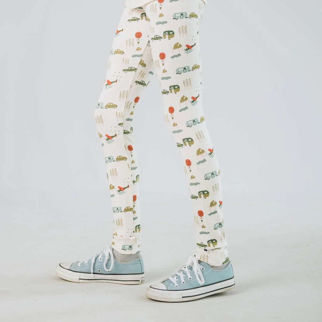 Child wearing white leggings with camping car print and blue sneakers on white background