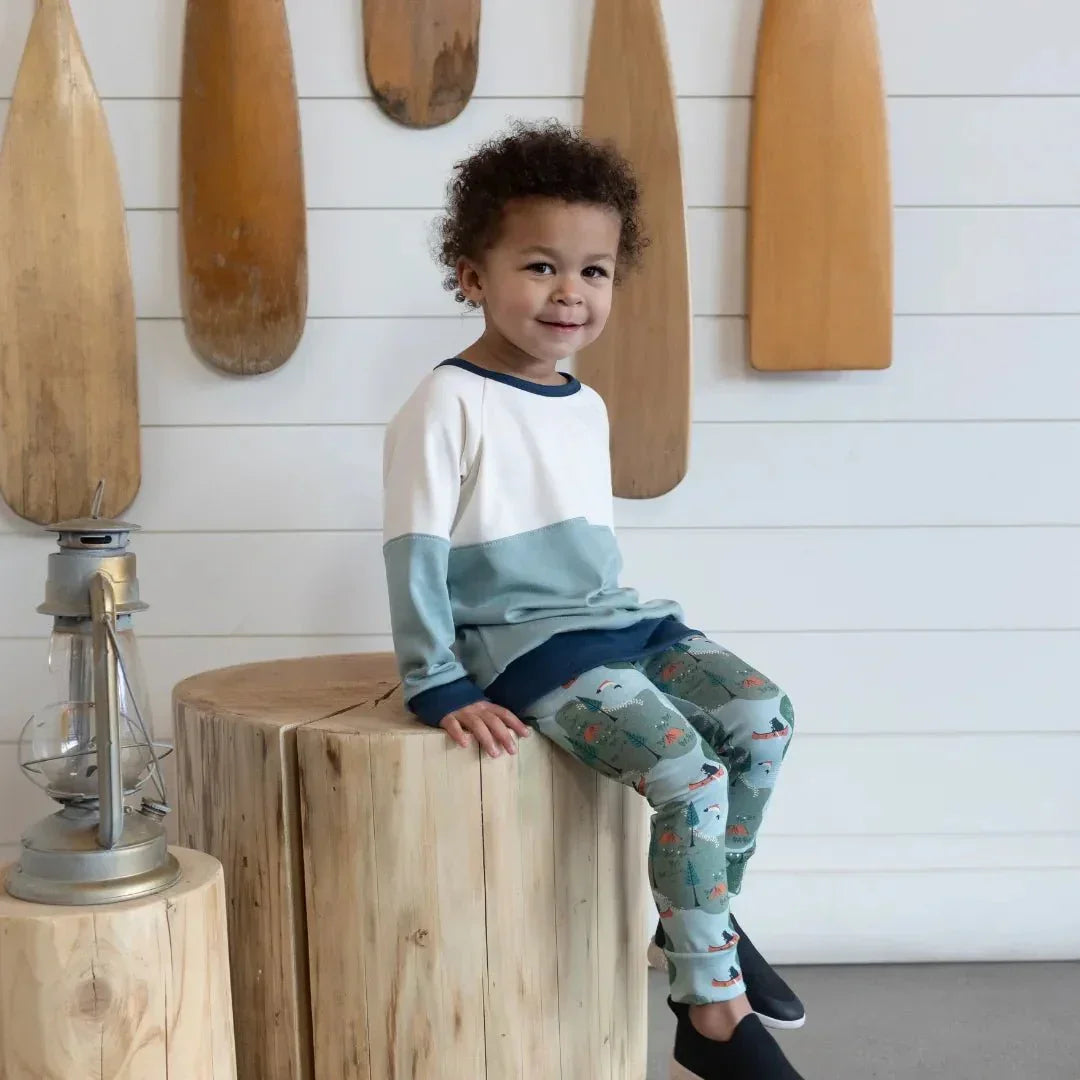 Kid wearing printed bamboo leggings and a color-block sweater, sitting on wood indoors