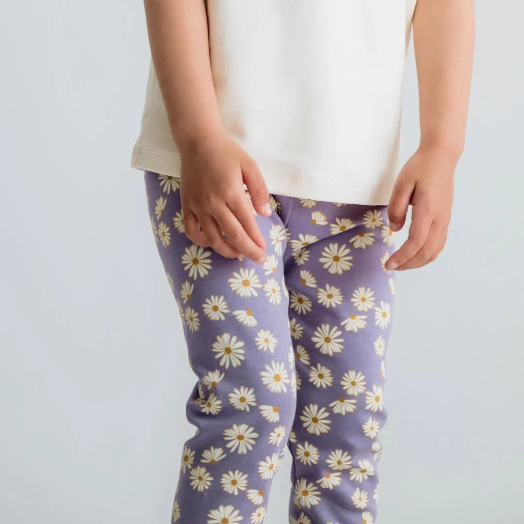 Child in cream shirt and purple daisy print leggings against plain background