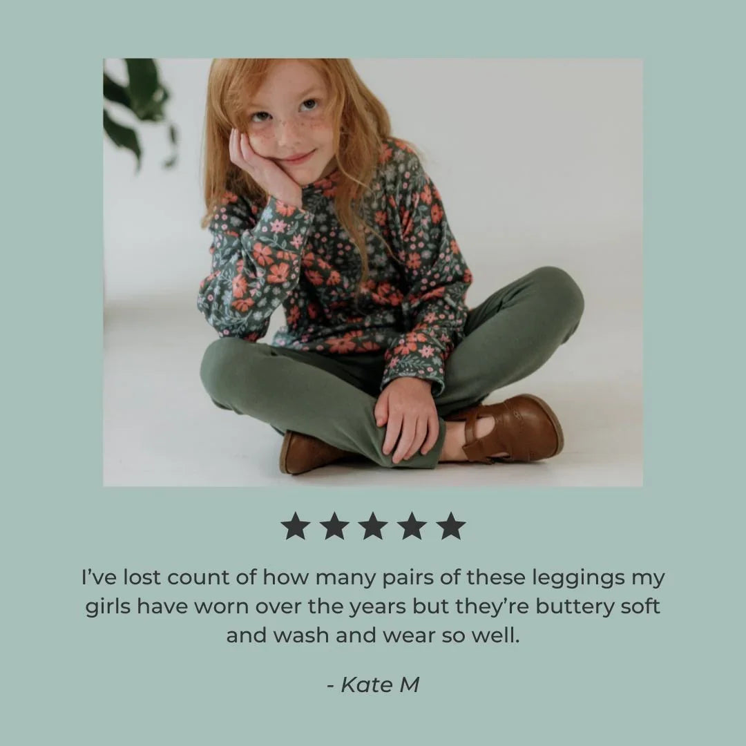 Girl wearing green bamboo leggings, floral top, and brown shoes sitting on floor