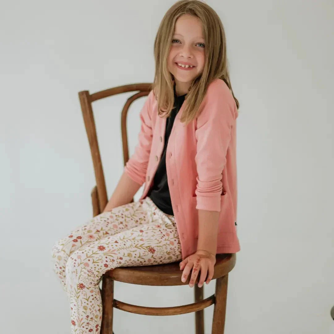 Girl wearing floral print bamboo leggings and pink cardigan sitting on wooden chair