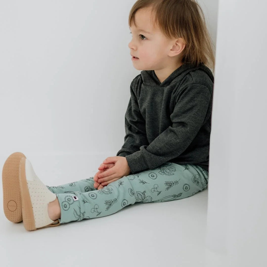Toddler wears bamboo leggings with botanical print and dark hoodie, sitting indoors