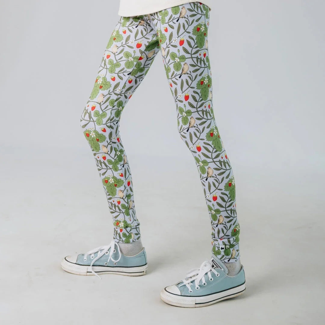 Child wearing botanical print leggings with strawberries and birds, blue sneakers, white background