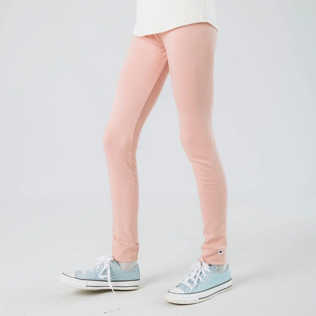 Youth wearing light pink bamboo leggings and blue sneakers on a white background