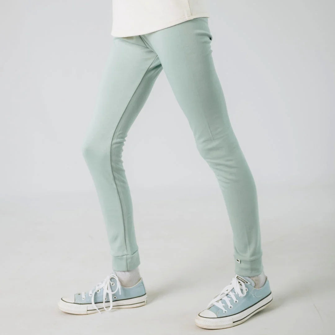 Light green kids leggings with cuffed ankles and pale blue sneakers on white background