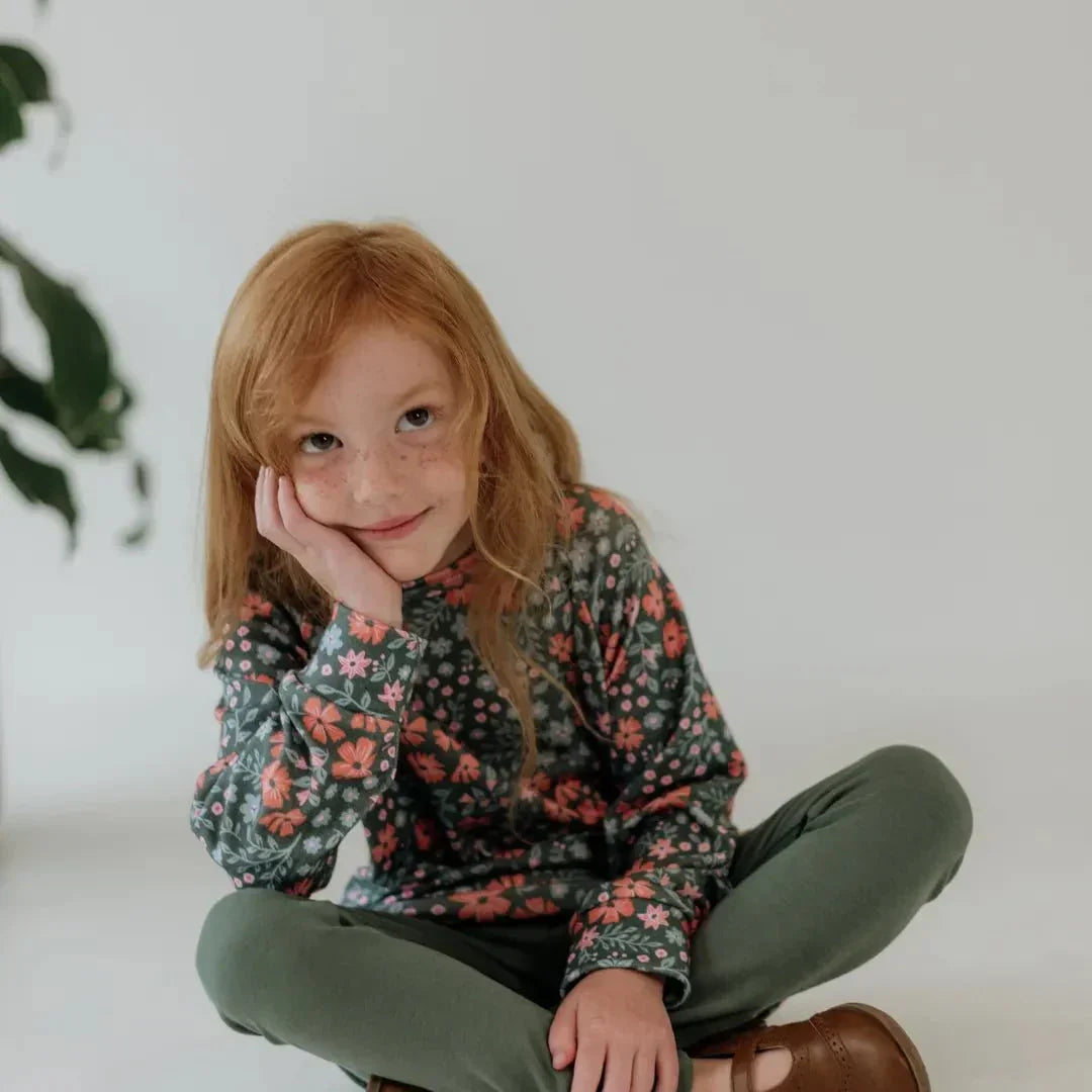 Girl in green bamboo leggings and floral top sitting on floor, casual kids fashion