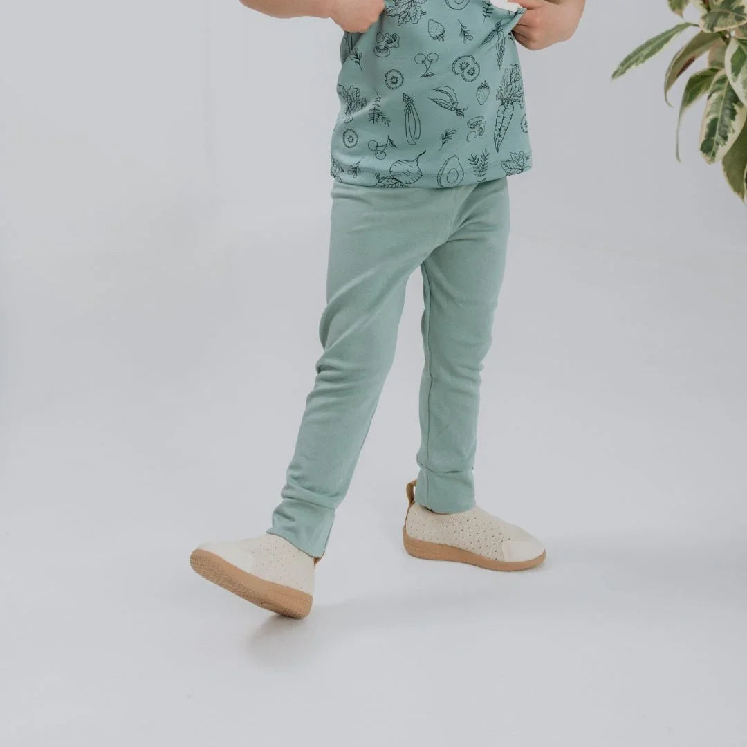 Toddler wearing mint bamboo leggings and beige shoes on white studio background