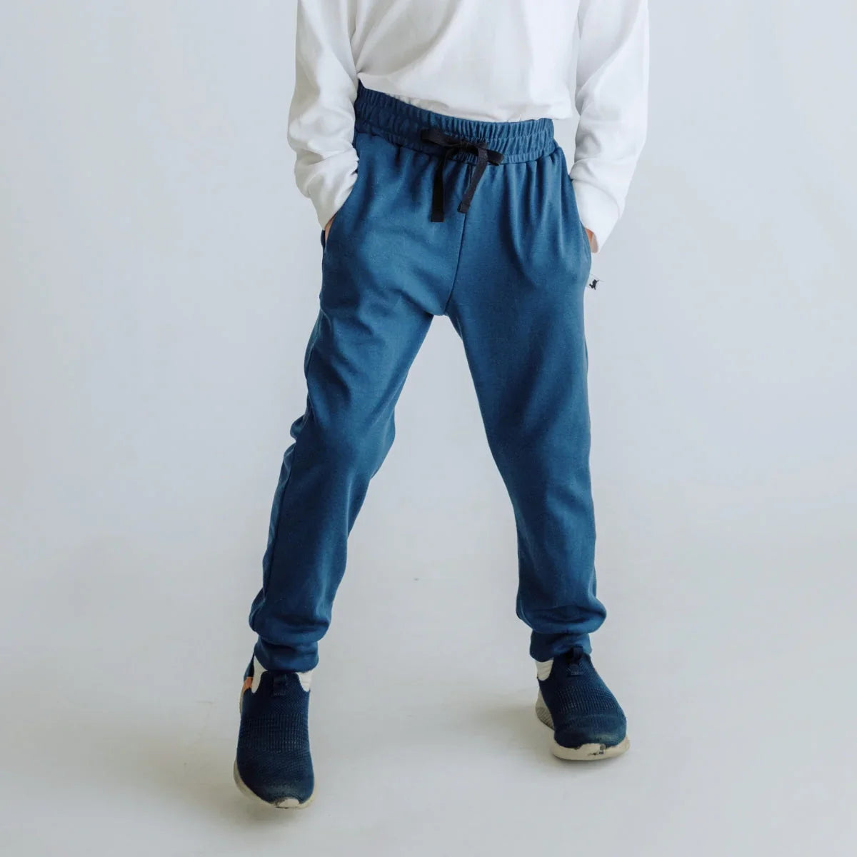 Child wearing blue jogger sweatpants and navy sneakers on white background