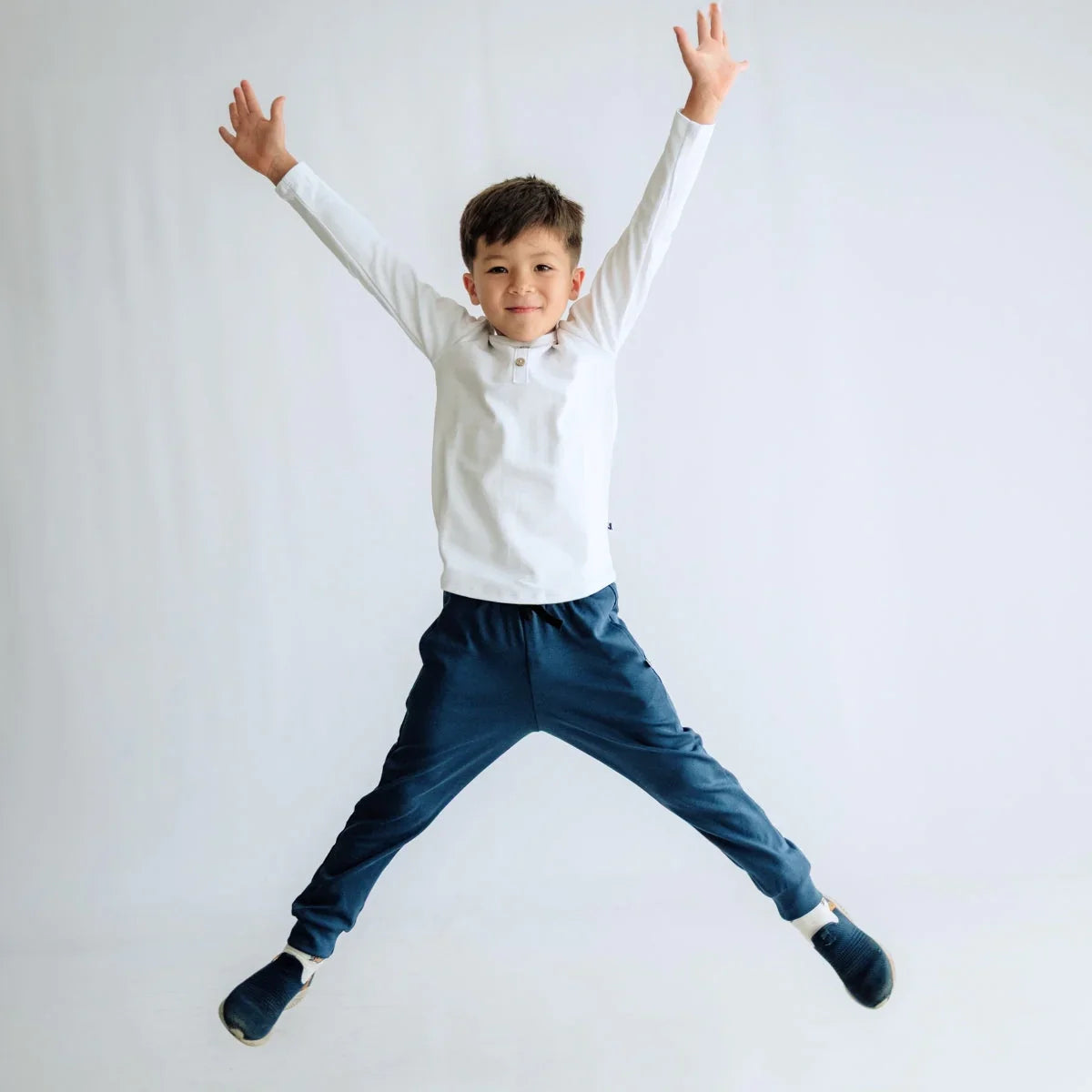 Smiling boy in white shirt and blue pants jumping against plain white background