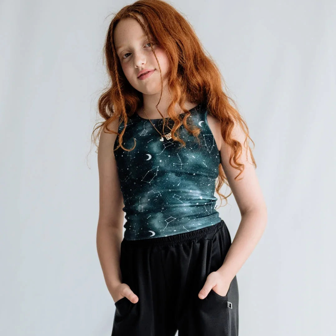 Red-haired girl wearing constellation print tank top and black pants on white background