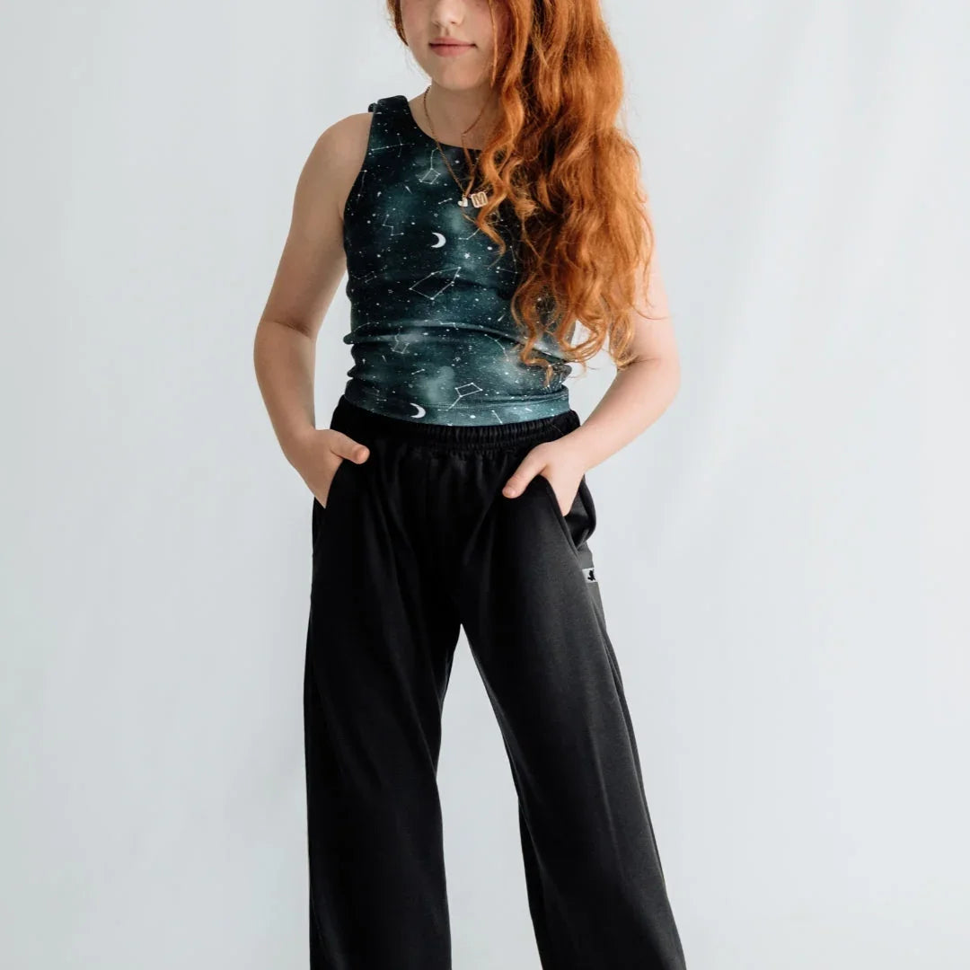 Girl in galaxy print tank top and black pants posing against light background