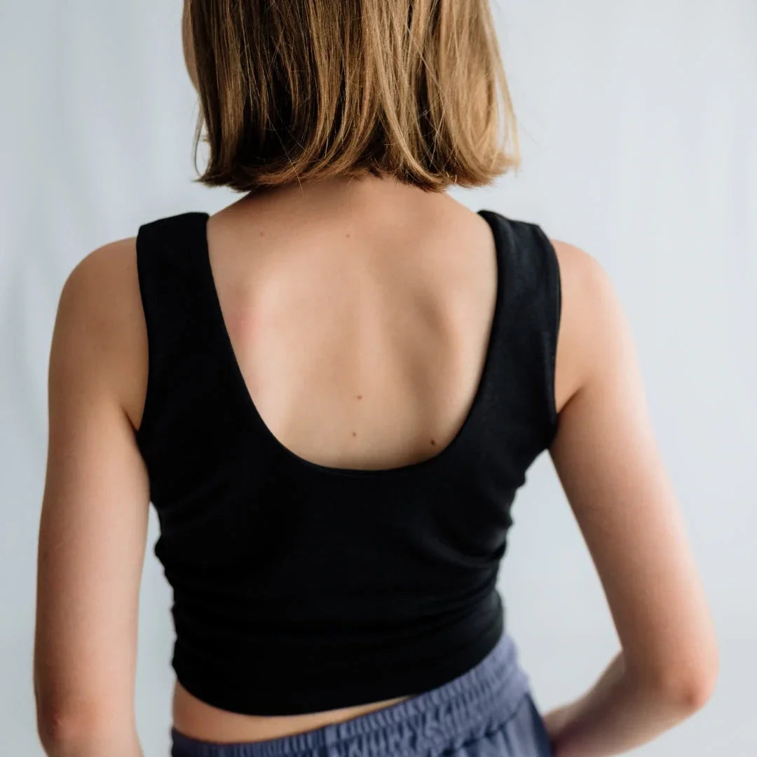 Woman in black sleeveless crop top with scooped back, short hair, standing indoors