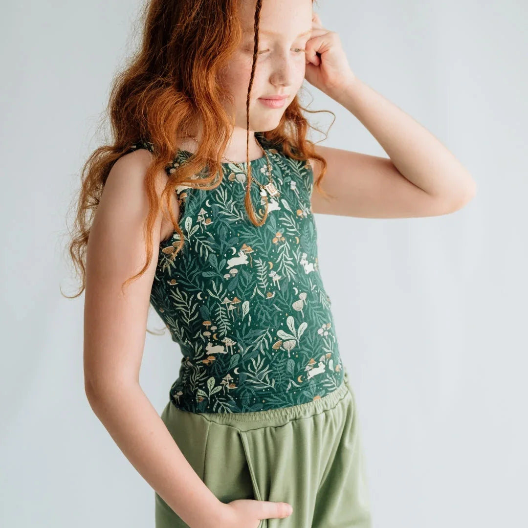 Girl in green floral sleeveless top and pants, hand in pocket, light background