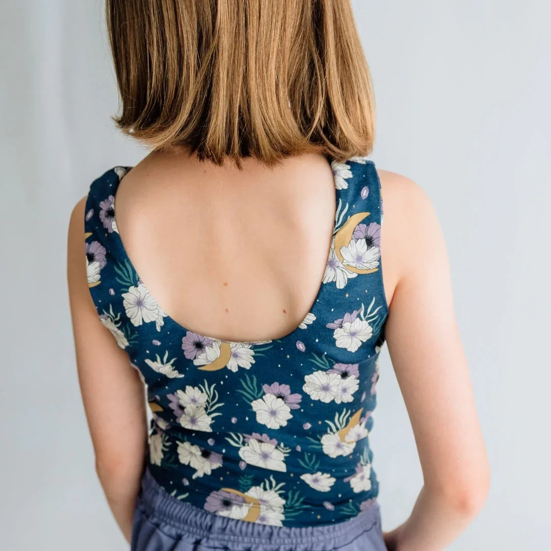 Girl in blue floral sleeveless top with open back, short hair, neutral background