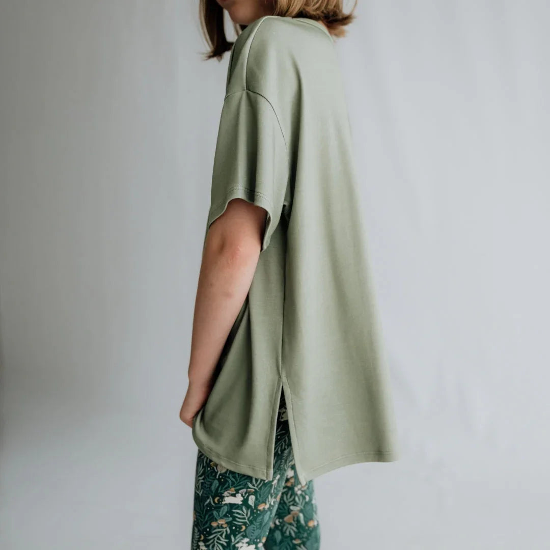 Woman in oversized sage green t-shirt and floral green pants, side view, neutral background