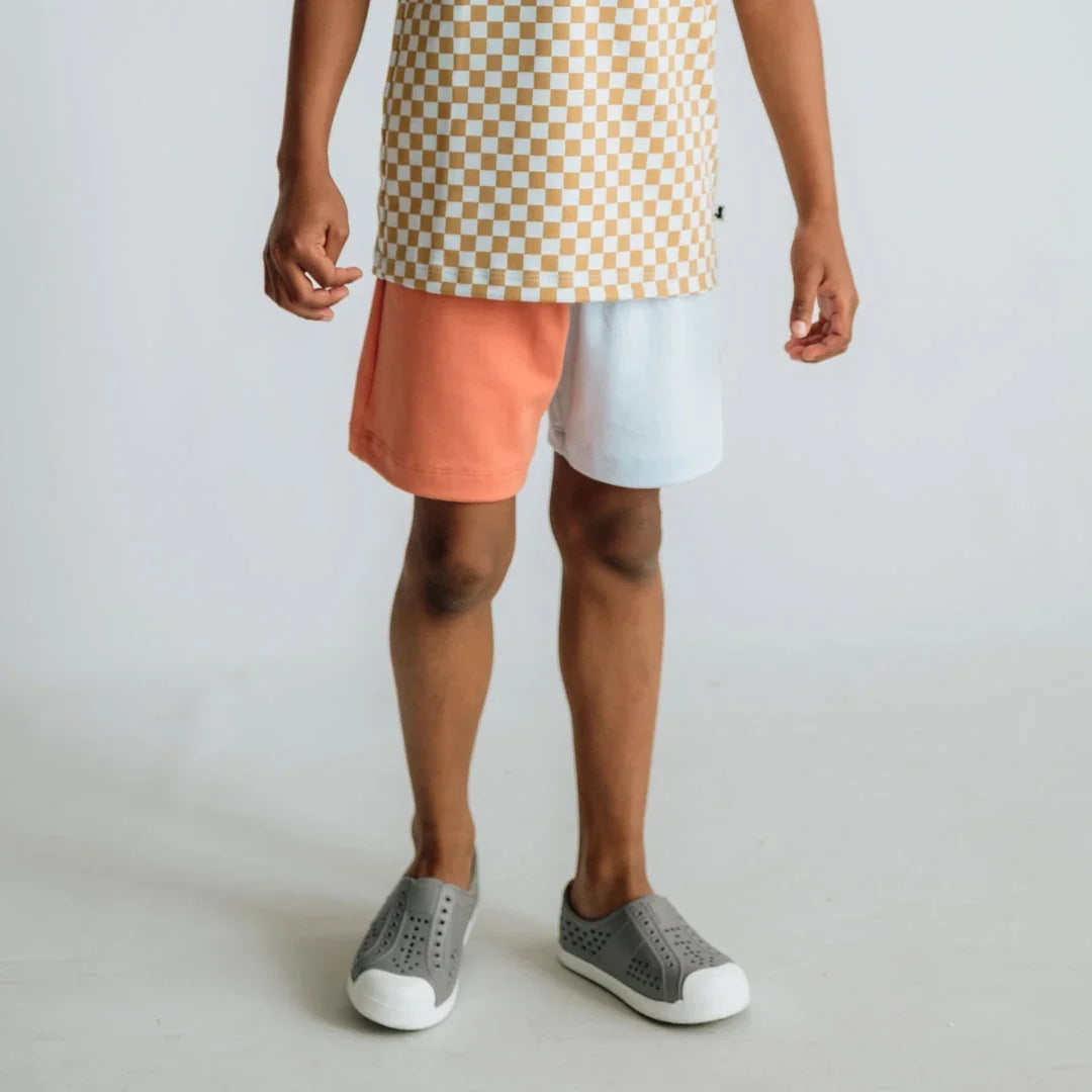 Child in checkered shirt, colorblock shorts, and gray slip-on shoes on white background