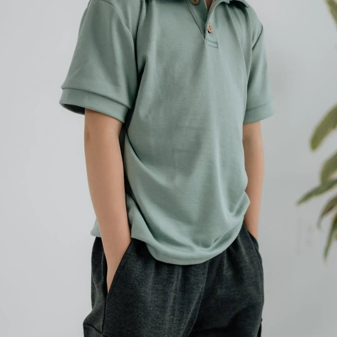 Youth wearing sage green bamboo polo shirt and dark shorts with hands in pockets